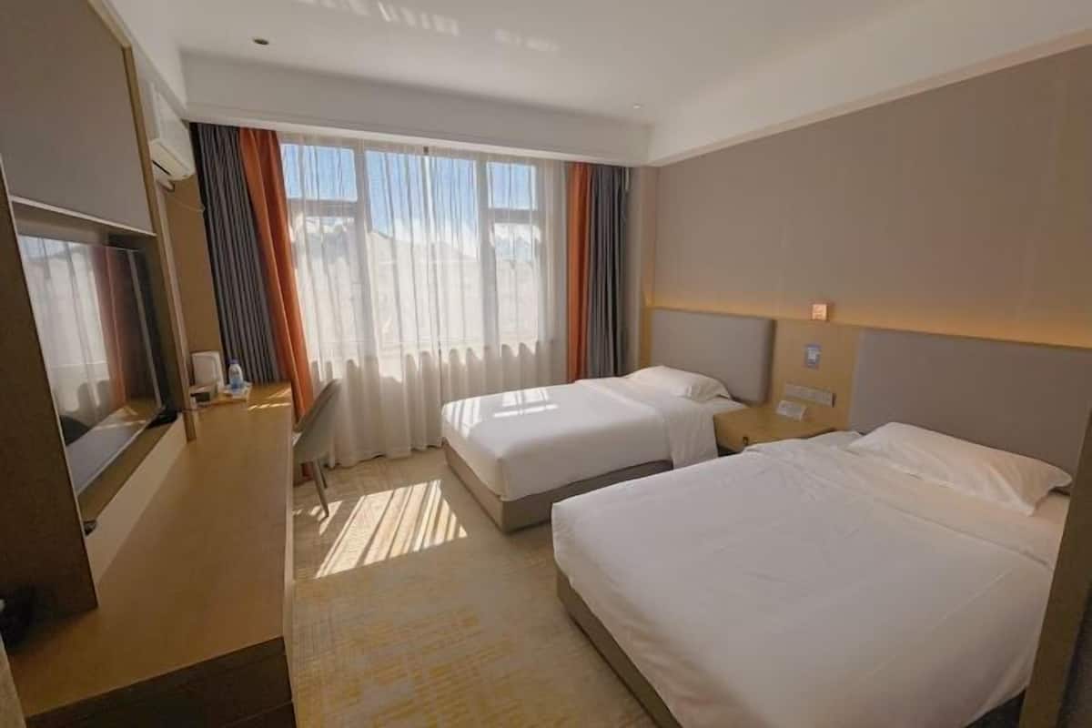 Habitación de hotel con dos camas, televisión, escritorio y ventana con cortinas.