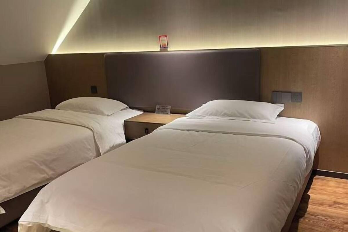 Una habitación de hotel con dos camas individuales, una mesita de noche, un reloj en la pared y una lámpara en el techo.