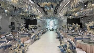 Un espacio con filas de mesas y sillas, un pasillo central y arreglos florales decorativos.