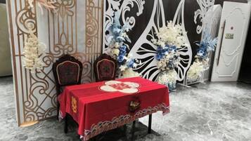 Una habitación con mantel rojo, dos sillas, un muro decorativo y un arreglo floral.