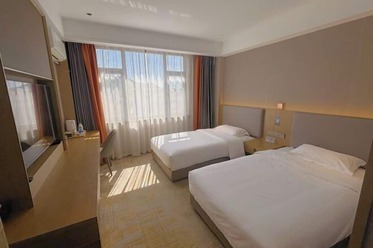 Habitación de hotel con dos camas, televisión, escritorio y ventana con cortinas.