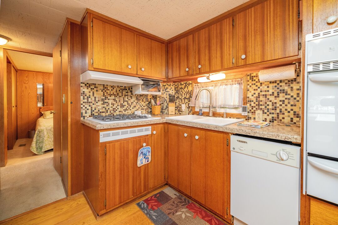 A compact kitchen with wooden cabinets, a white dishwasher, and a tiled backsplash.