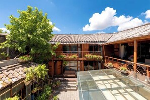 A traditional courtyard with a wooden building, a glass table, and potted plants. - Lijiang Wuge Inn (Lijiang)