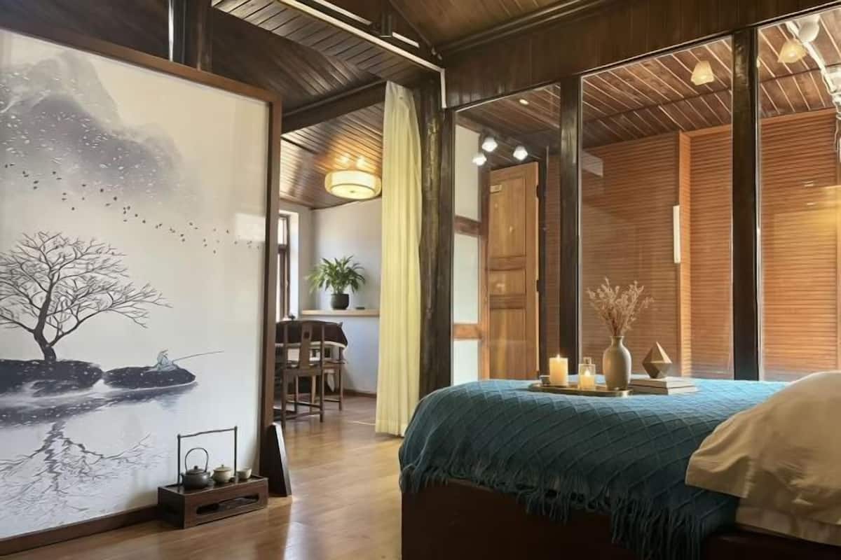 A room with a bed, a painting, a desk, and a chair.