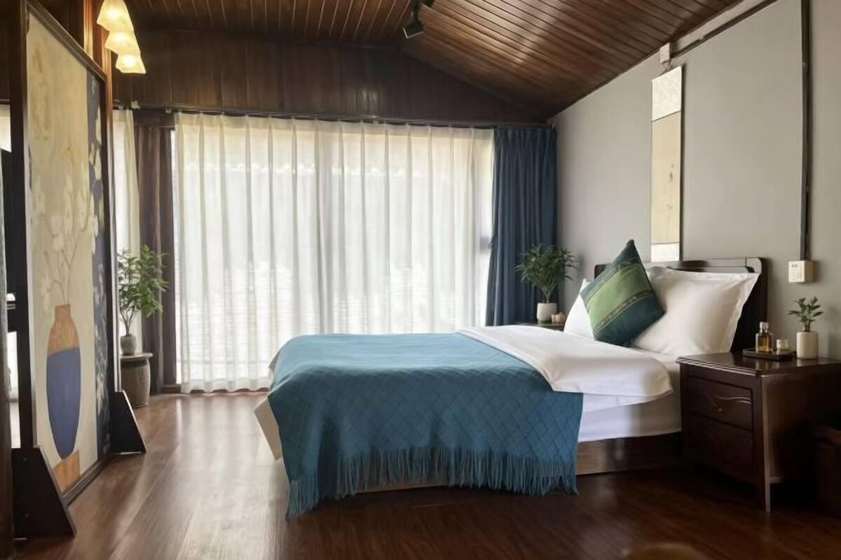 A bedroom with a bed, nightstands, a window with curtains, and a wooden ceiling.