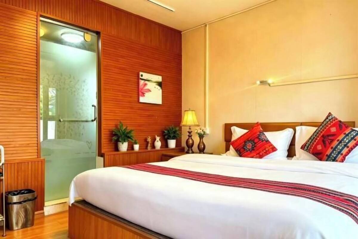 A hotel room with a bed, wooden paneling, a nightstand with a lamp, and a window with a view.