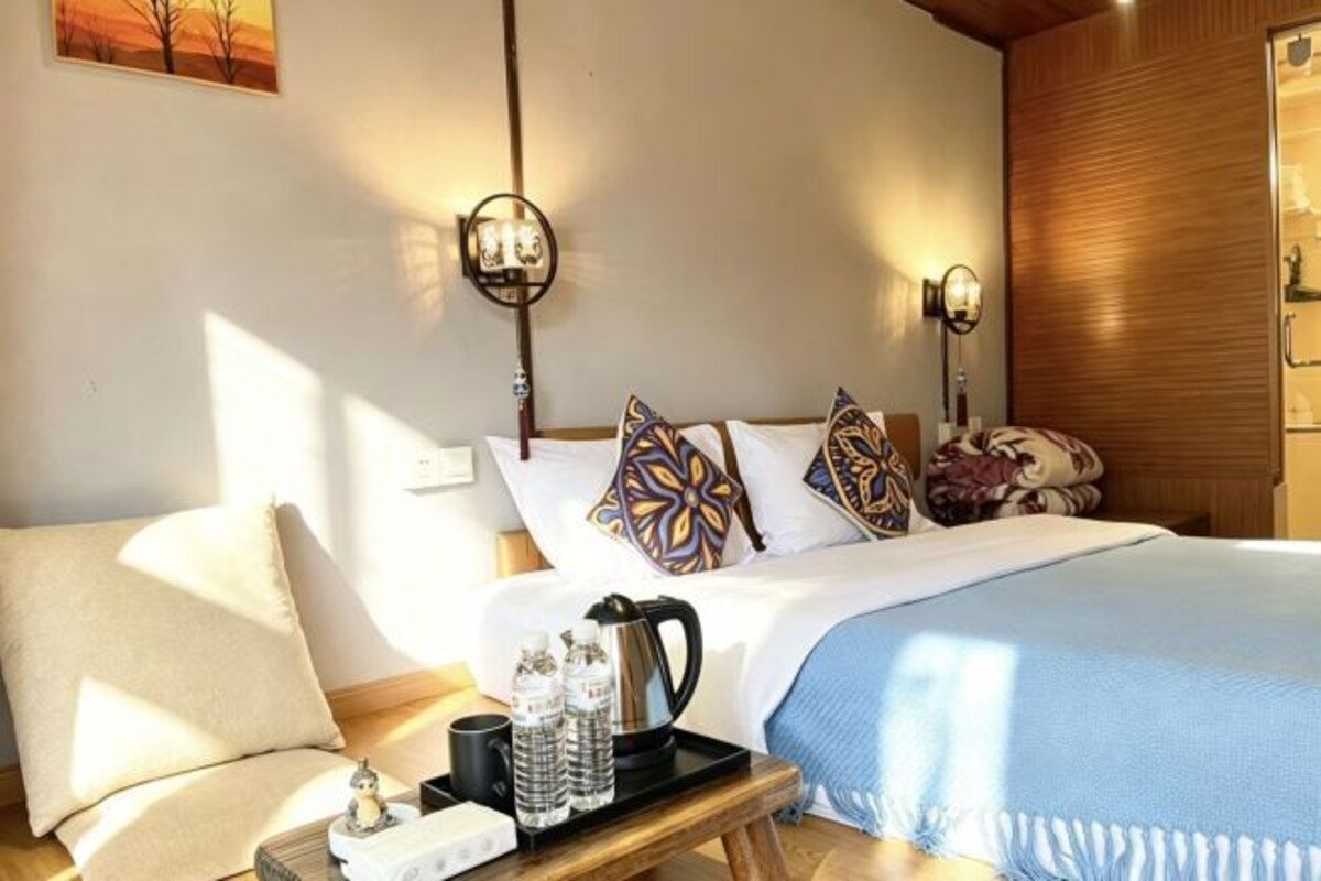A hotel room with a bed, bedside lamps, a bedside table with a tray, and a window.