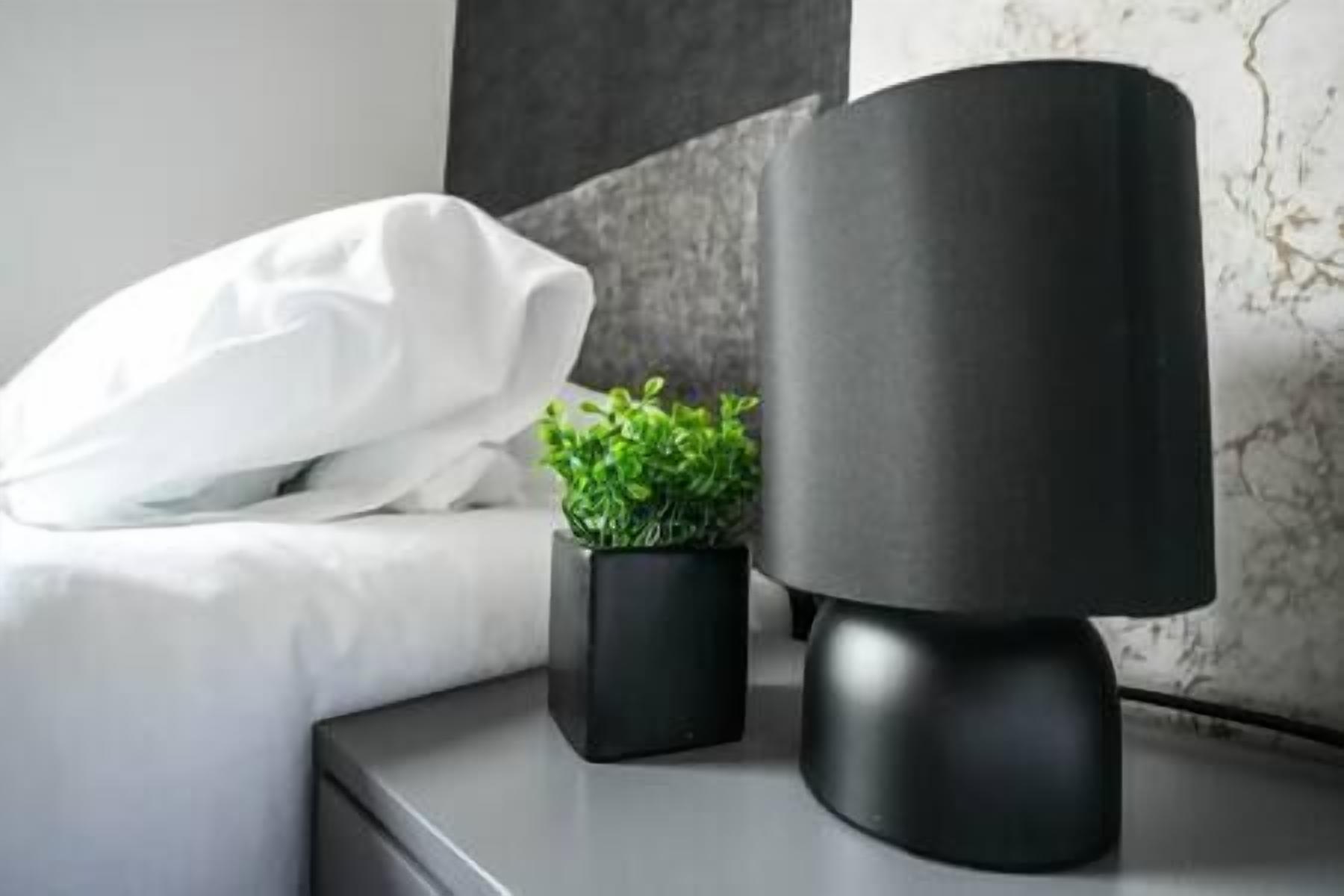 A neatly made bed with white bedding, a small potted plant, and a modern black lamp on a bedside table.