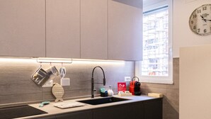 A modern kitchen with a built-in sink, a clock on the wall, and a window with a view of the city. - Casa Rattazzi by Wonderful Italy (Albisola Superiore)