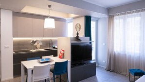 A modern hotel room with a kitchenette, a dining area with a table and chairs, a flat-screen TV, and a large window with curtains. - Casa Rattazzi by Wonderful Italy (Albisola Superiore)