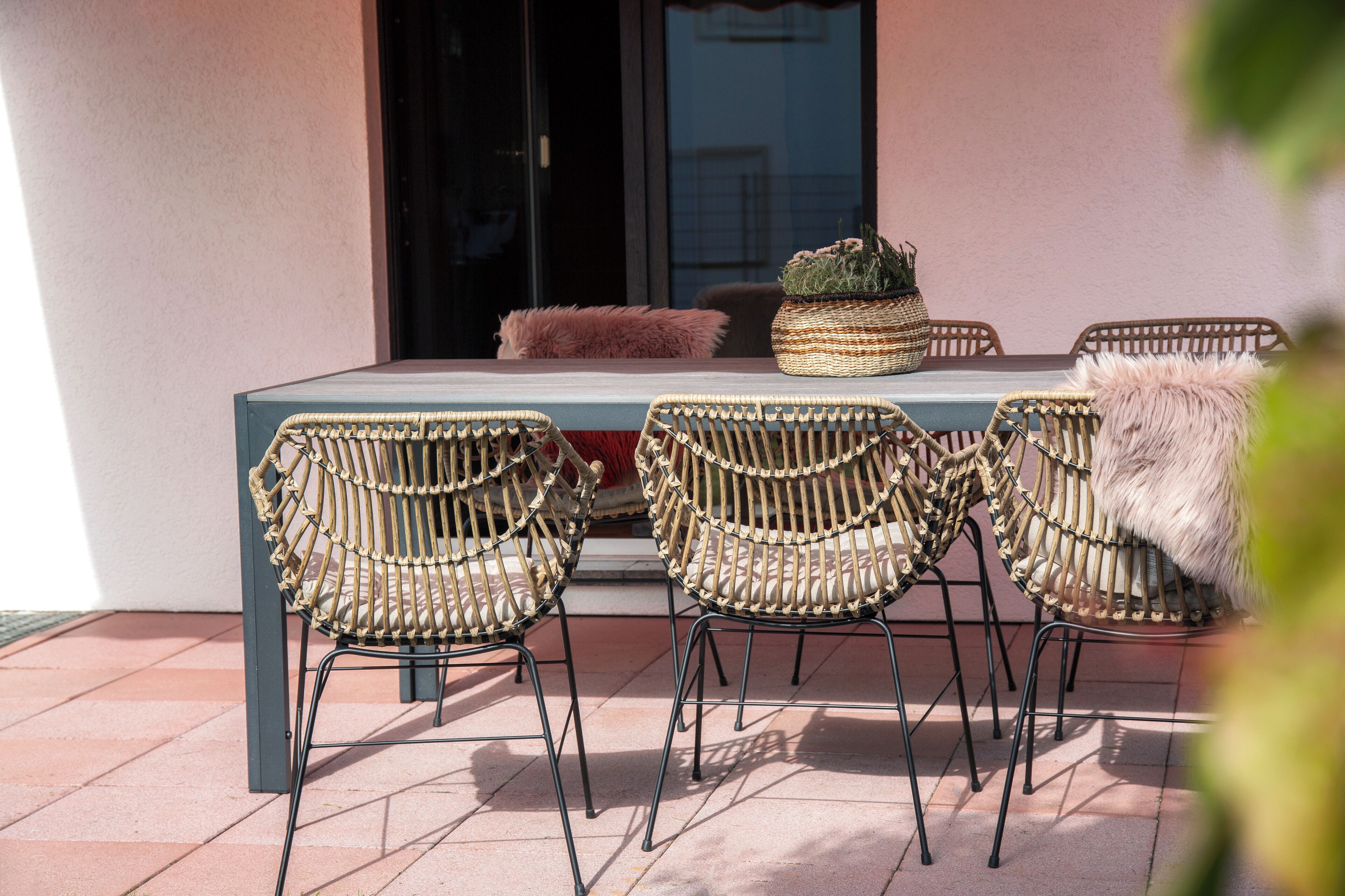 A patio with wicker chairs and a table, a potted plant, and a fluffy cushion.