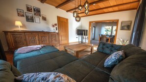 A spacious living room with a large sectional sofa, wooden ceiling beams, and a dining area in the background. - Gemütliche Ferienwohnung in der Vulkaneifel Casa Oos (Rockeskyll)