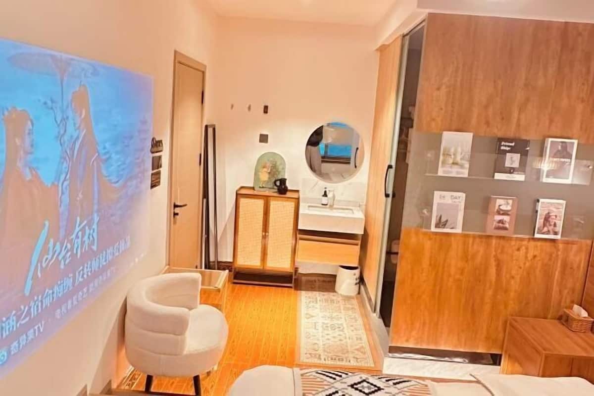 A modern hotel room with a projection screen displaying a scenic image, a comfortable seating area, a wooden cabinet, and a small table with a mirror.