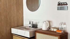 Une salle de bain moderne avec un meuble-lavabo en bois, un évier et un miroir. On y trouve des articles de toilette et une machine à café sur le meuble-lavabo.