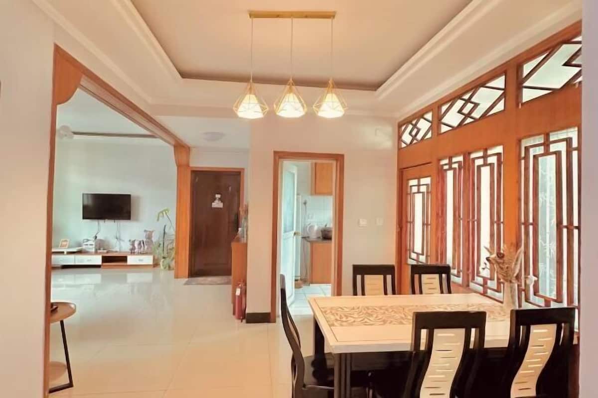 A dining area with a table and chairs, a television mounted on the wall, and a kitchen visible through an open door.