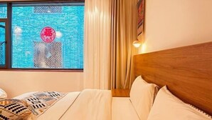 Une chambre d’hôtel avec une grande fenêtre, un lit avec une literie à motifs et une tête de lit en bois.