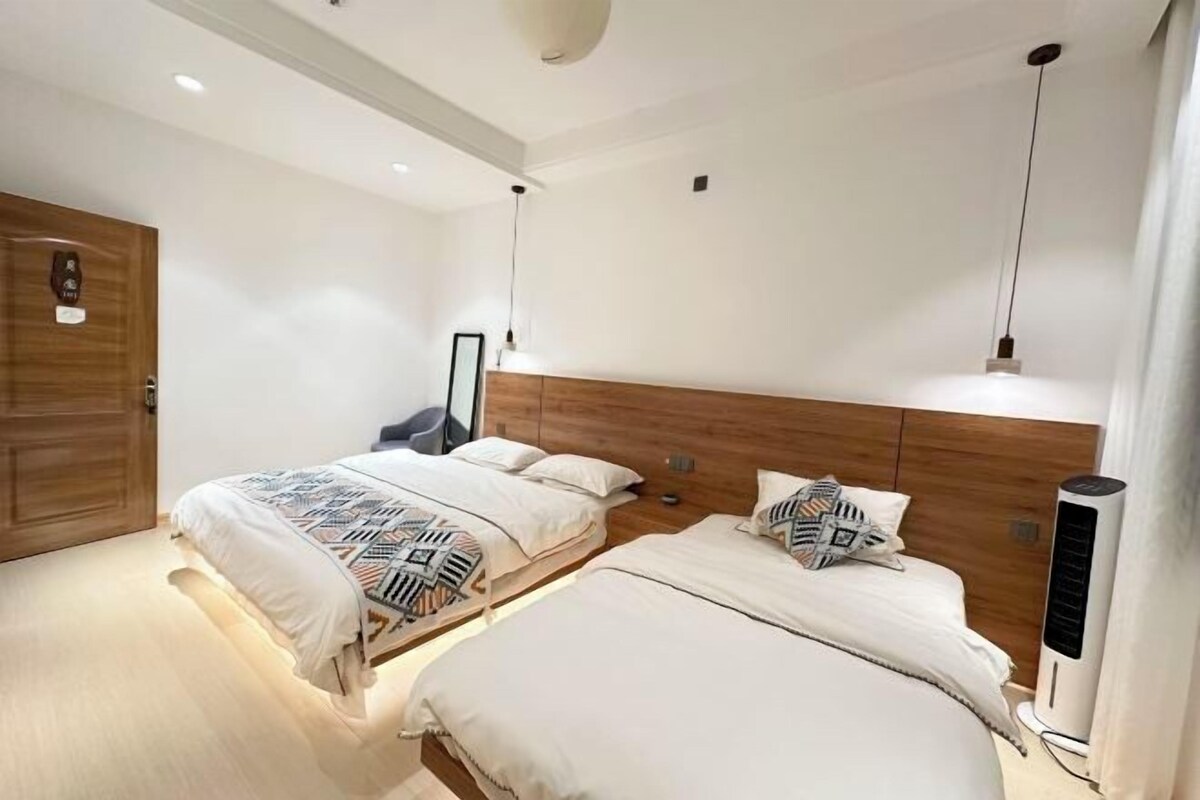 Une chambre d’hôtel moderne avec deux lits, une tête de lit en bois, une table de chevet, un miroir et un climatiseur fixé au mur.