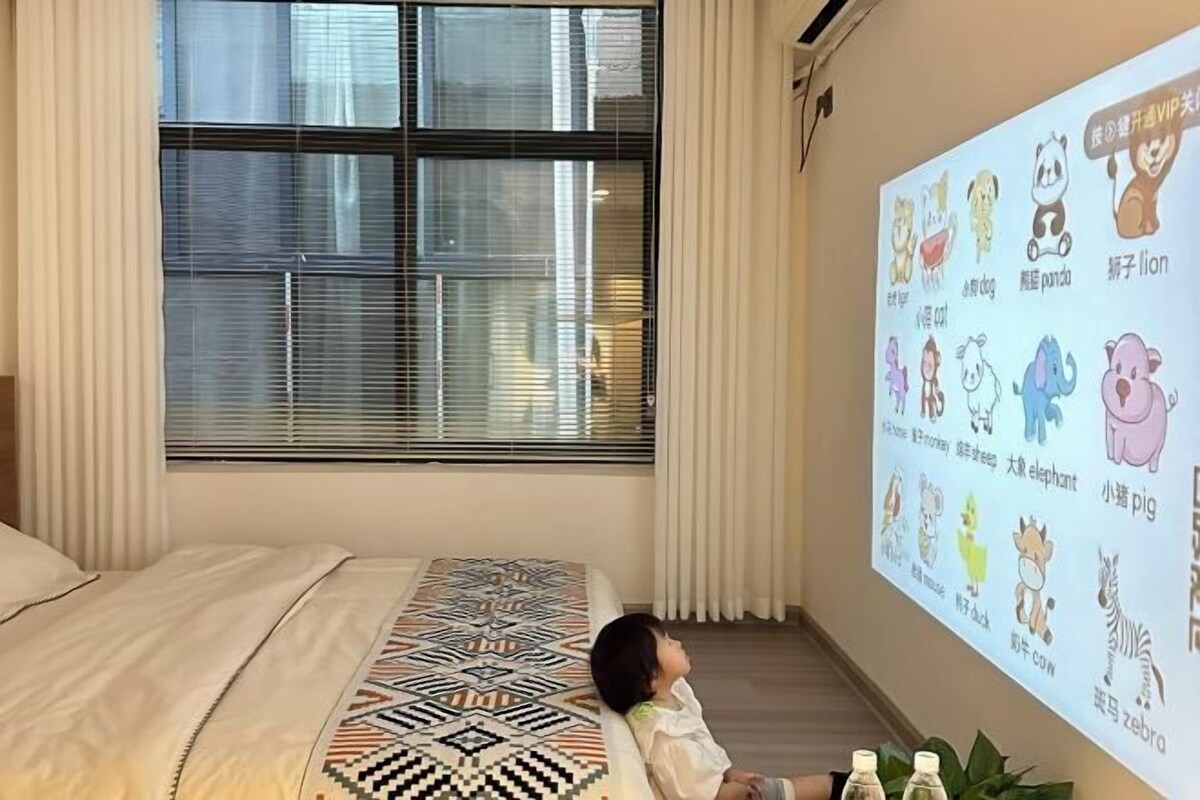 Un enfant allongé sur un lit recouvert d’une couverture à motifs, un écran de projection affichant des illustrations d’animaux et une fenêtre avec des stores.