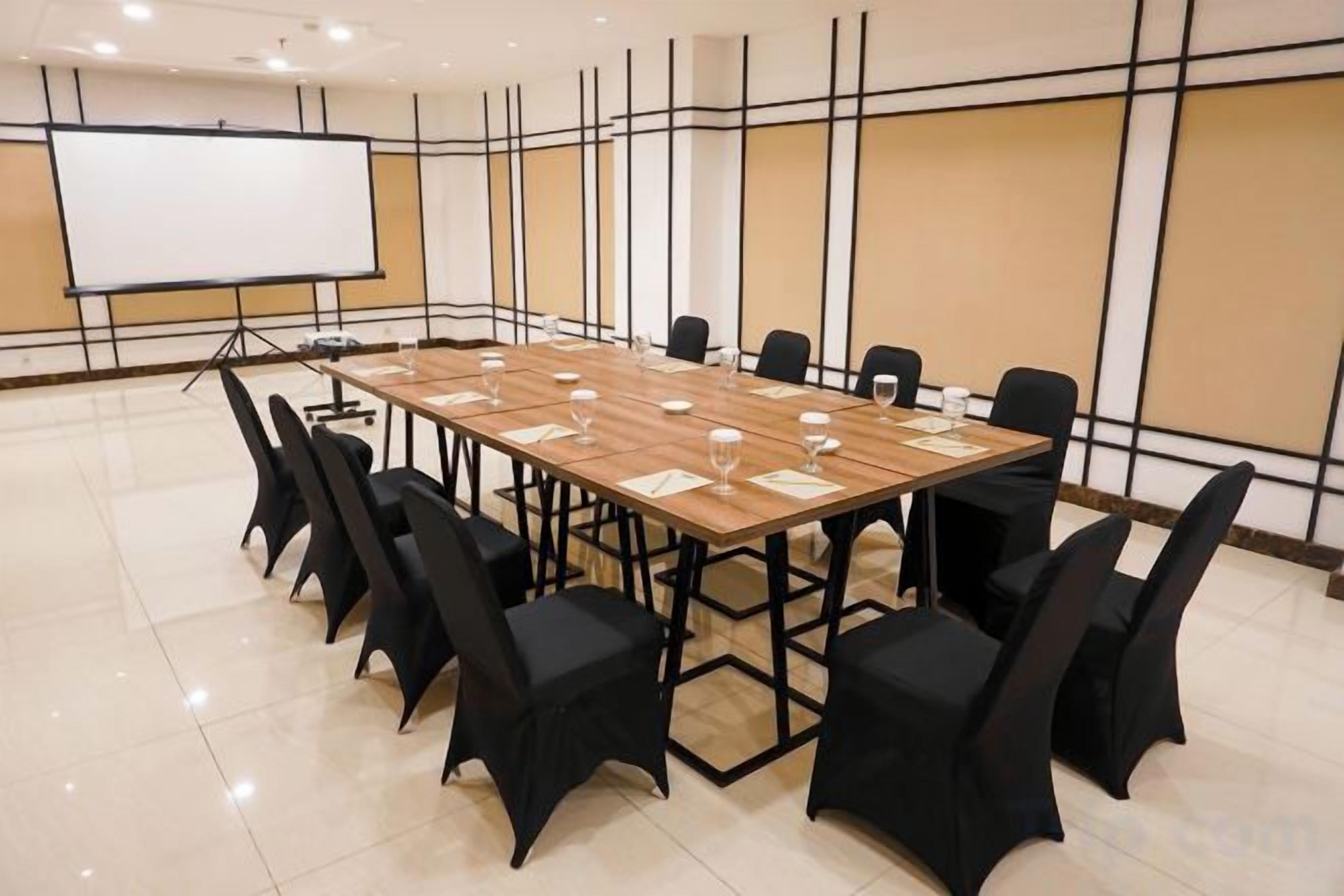 Une salle de conférence avec une longue table, des chaises noires et un tableau blanc.