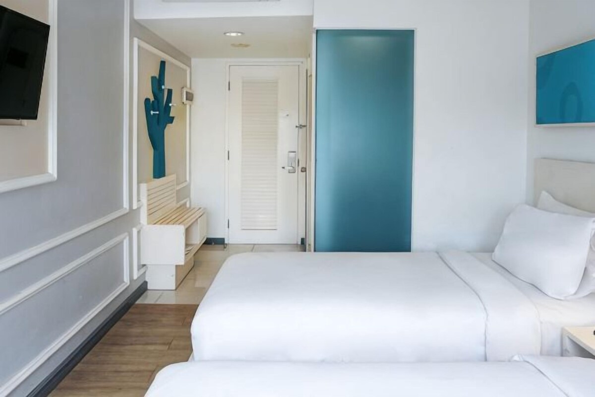 Ett hotellrum med en säng, en bänk, en dörr och en tv på väggen.