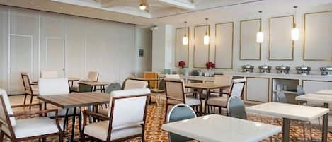 Ein Hotel-Speisesaal mit mehreren Tischen und Stühlen, einem Buffet und einem gemusterten Teppich.