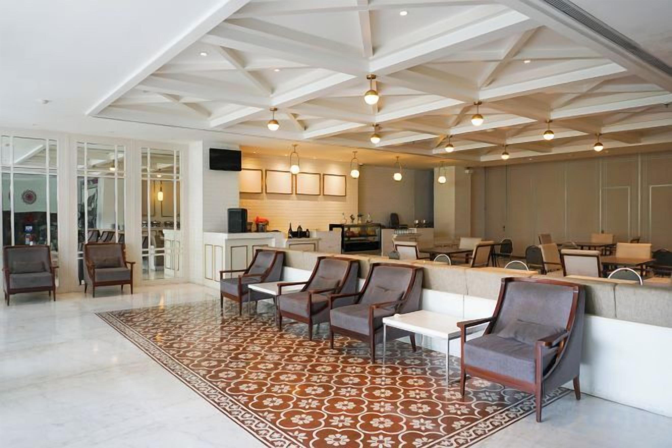 A spacious living area with a high ceiling, a kitchen in the background, and a patterned rug.