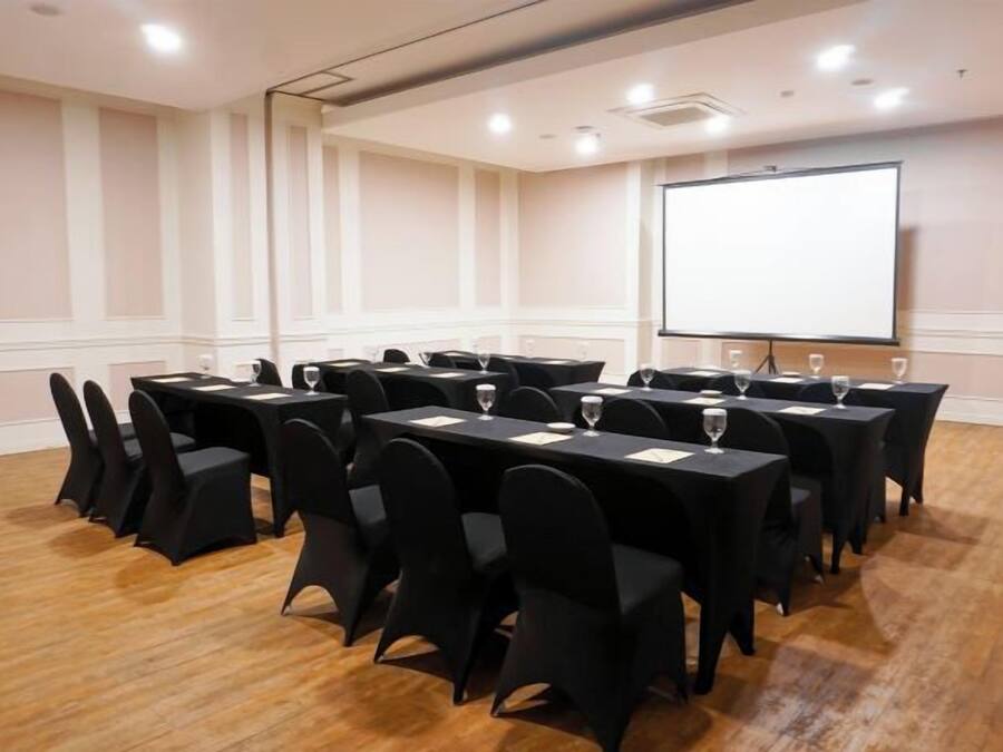 Un salón de conferencias con varias mesas y sillas, una pantalla de proyector y suelo de madera.