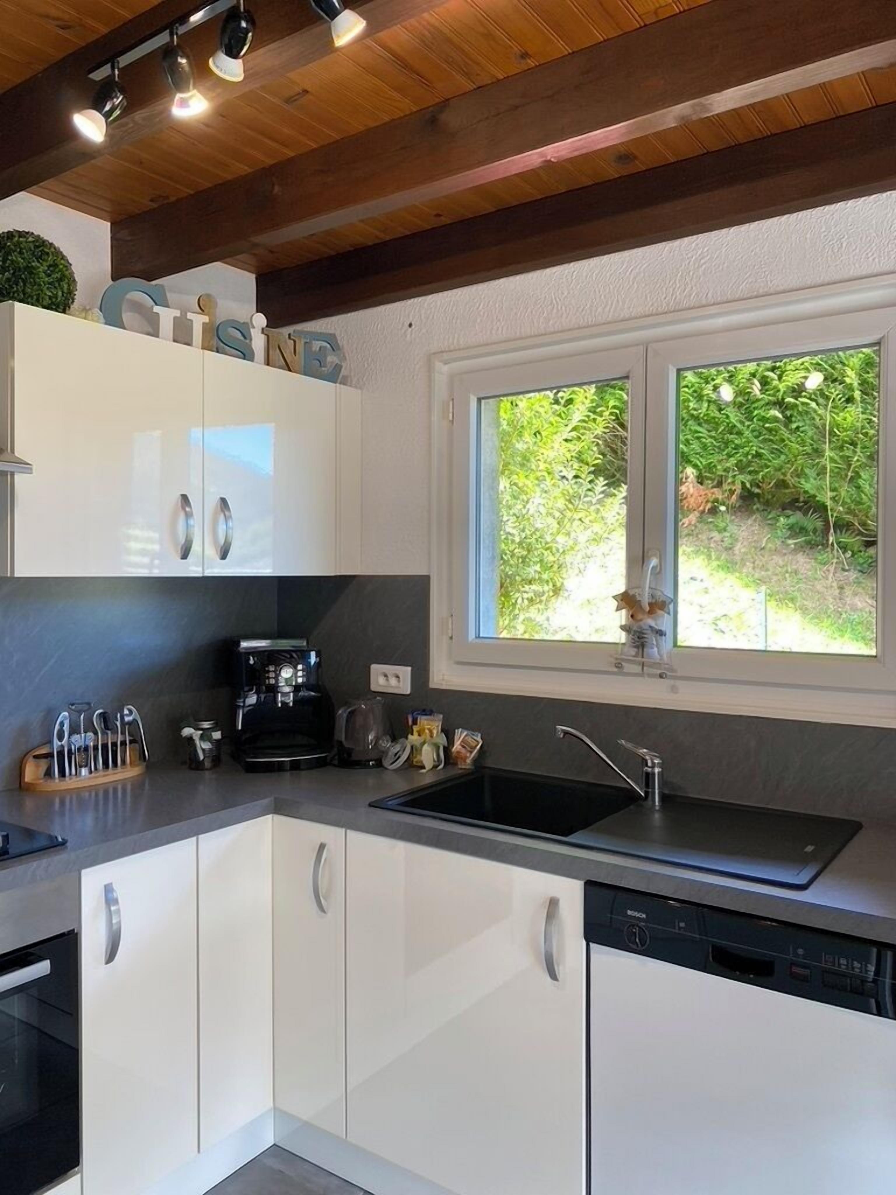 A modern kitchen with white cabinets, a Bosch dishwasher, a coffee maker, and a window with a view of greenery.