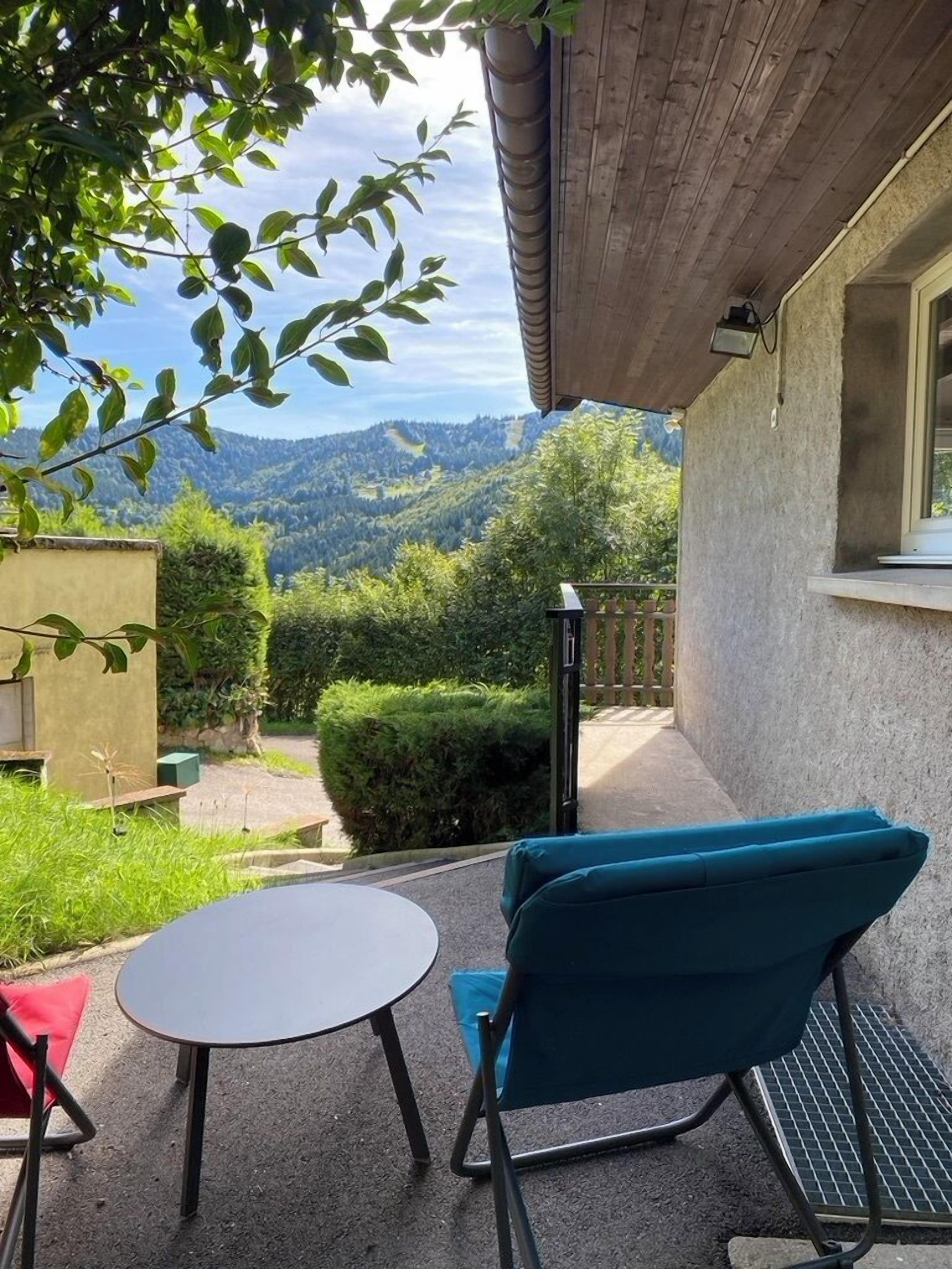 A patio with a table and chairs, a view of mountains, and a building with a window.