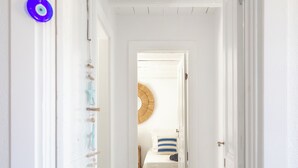 Un couloir étroit mène à une chambre où se trouvent un lit, un miroir rond et une porte dotée d’une poignée en corde.