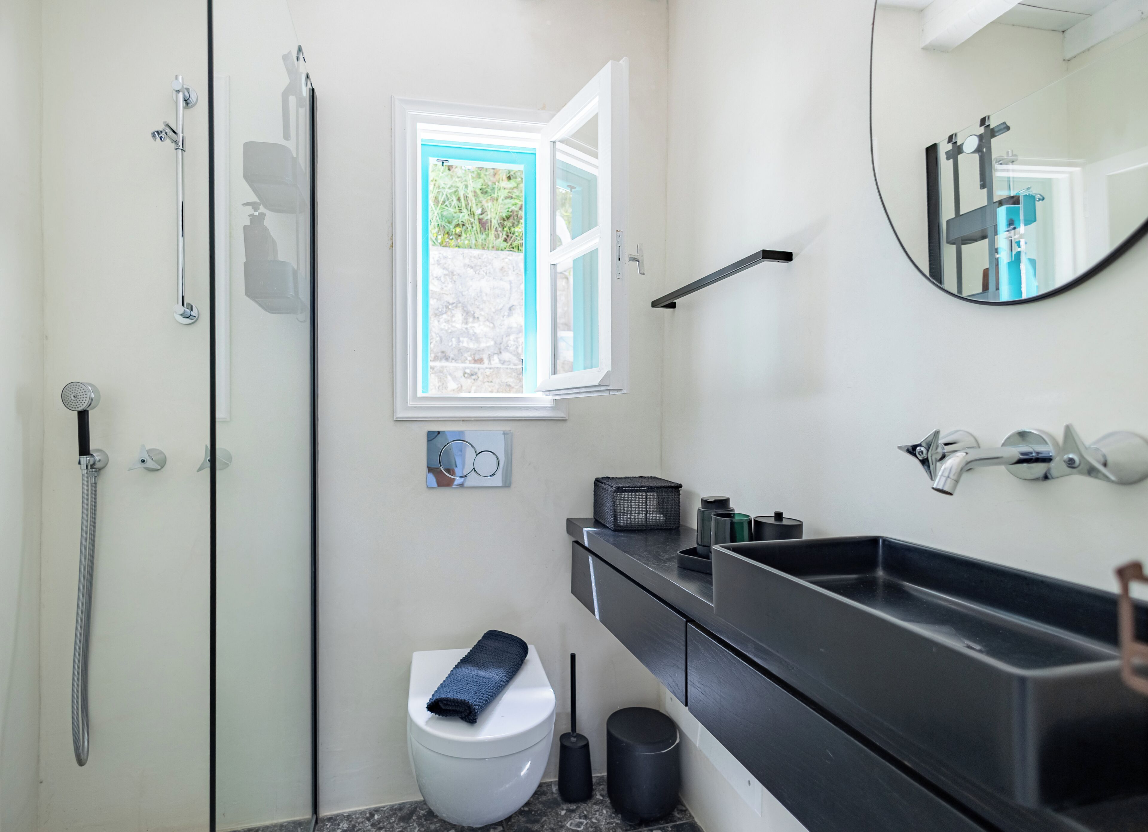 A bathroom with a shower, toilet, sink, and a window with an open door.