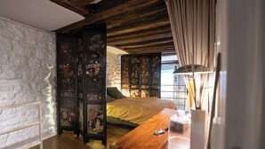 A bedroom with a wooden bed, a nightstand, a lamp, and a decorative screen with artwork. - Your stay in the heart of Paris in a large duplex apartment. Saint Germain (Paris)