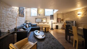 A modern living room with a stone wall, a black leather sofa, a wooden dining table, and a large window. - Your stay in the heart of Paris in a large duplex apartment. Saint Germain (Paris)