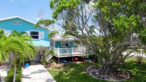 Une maison turquoise dotée d’une terrasse, entourée d’arbres et d’un petit jardin.