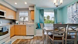 Une cuisine compacte avec des meubles en bois, un four à micro-ondes, un grille-pain et un évier. On y trouve également un coin repas avec une table et des chaises, et une vue sur la verdure environnante.