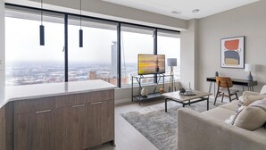 A modern living room with a large window, a flat-screen TV, a desk, and a sofa.