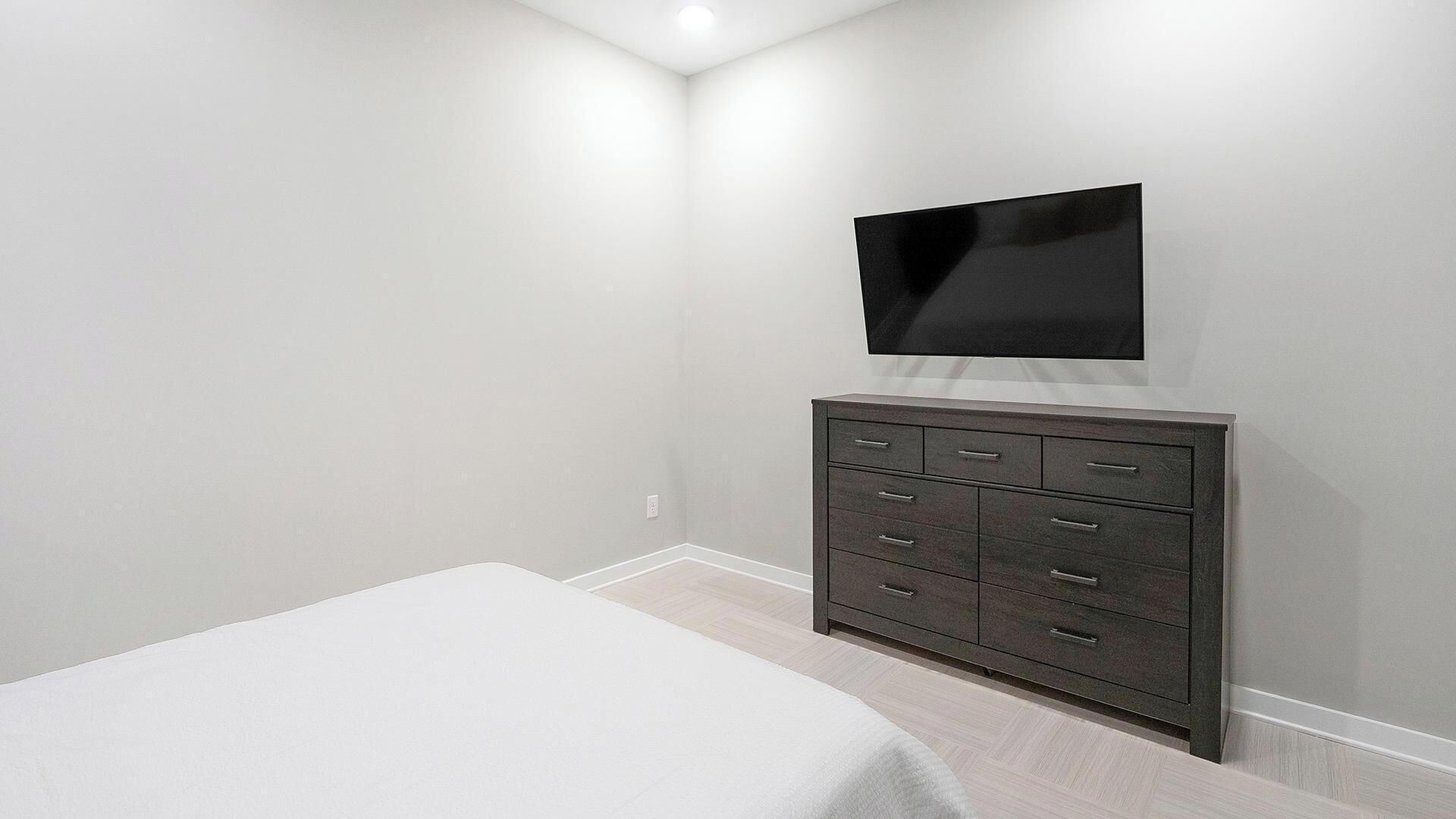 Een slaapkamer met een bed, een dressoir en een aan de muur bevestigde televisie.