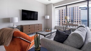 A modern living room with a sofa, a coffee table, a TV, and a large window with a city view.