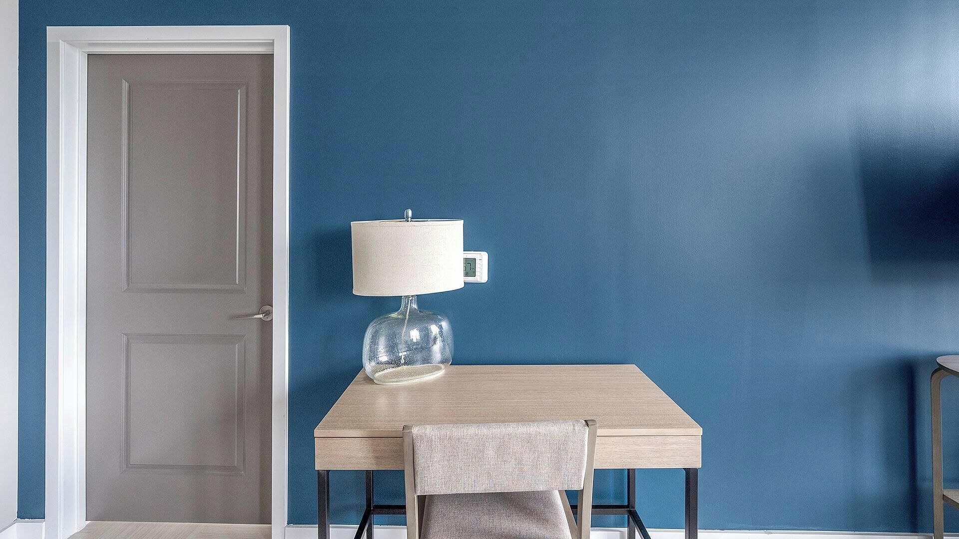 Una habitación con pared azul, una mesa de madera, una silla y una lámpara.