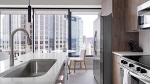 A modern kitchen with a stainless steel sink, a built-in oven, and a view of tall buildings through large windows.