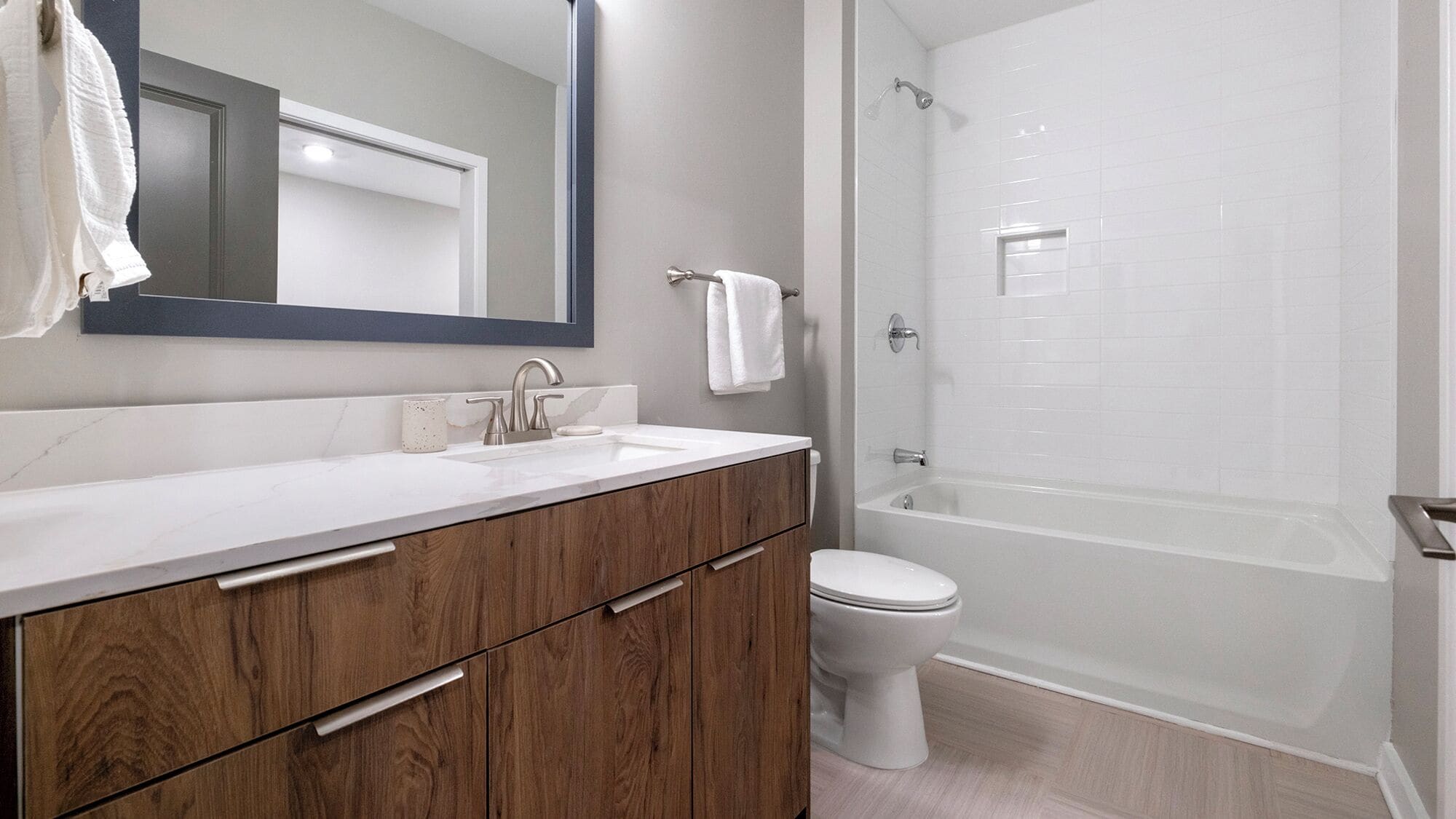 A modern bathroom with a wooden vanity, a white sink, a toilet, and a walk-in shower.
