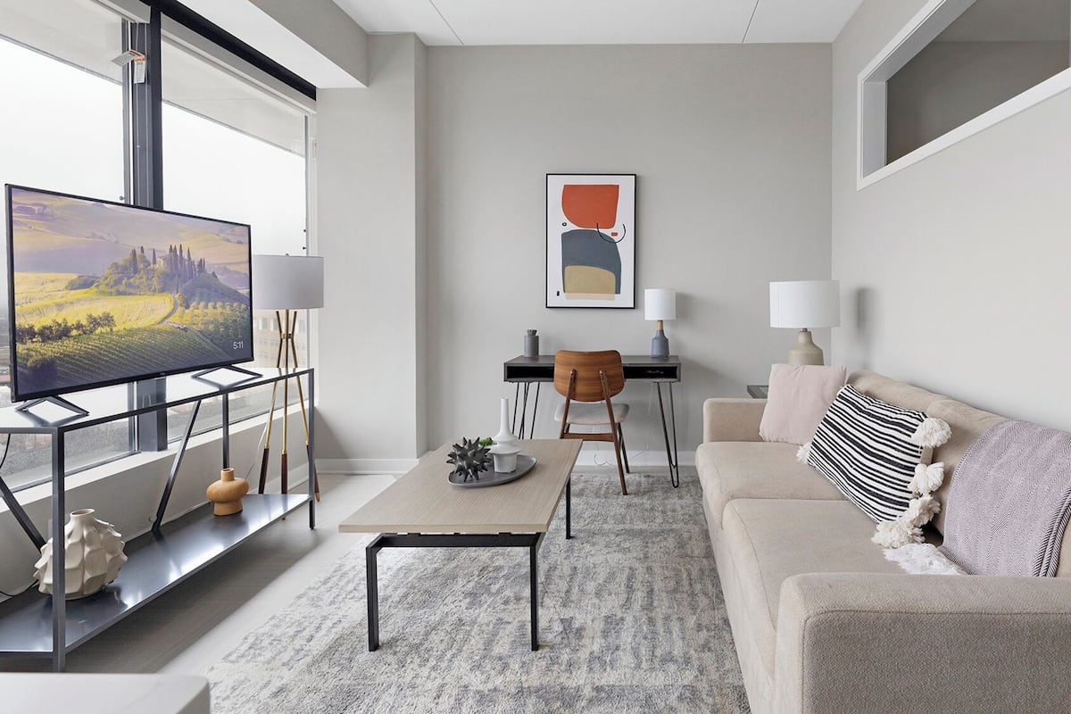 Una sala de estar moderna con un televisor de pantalla plana grande, una mesa de centro de madera, un sofá color beige y un escritorio con una silla.