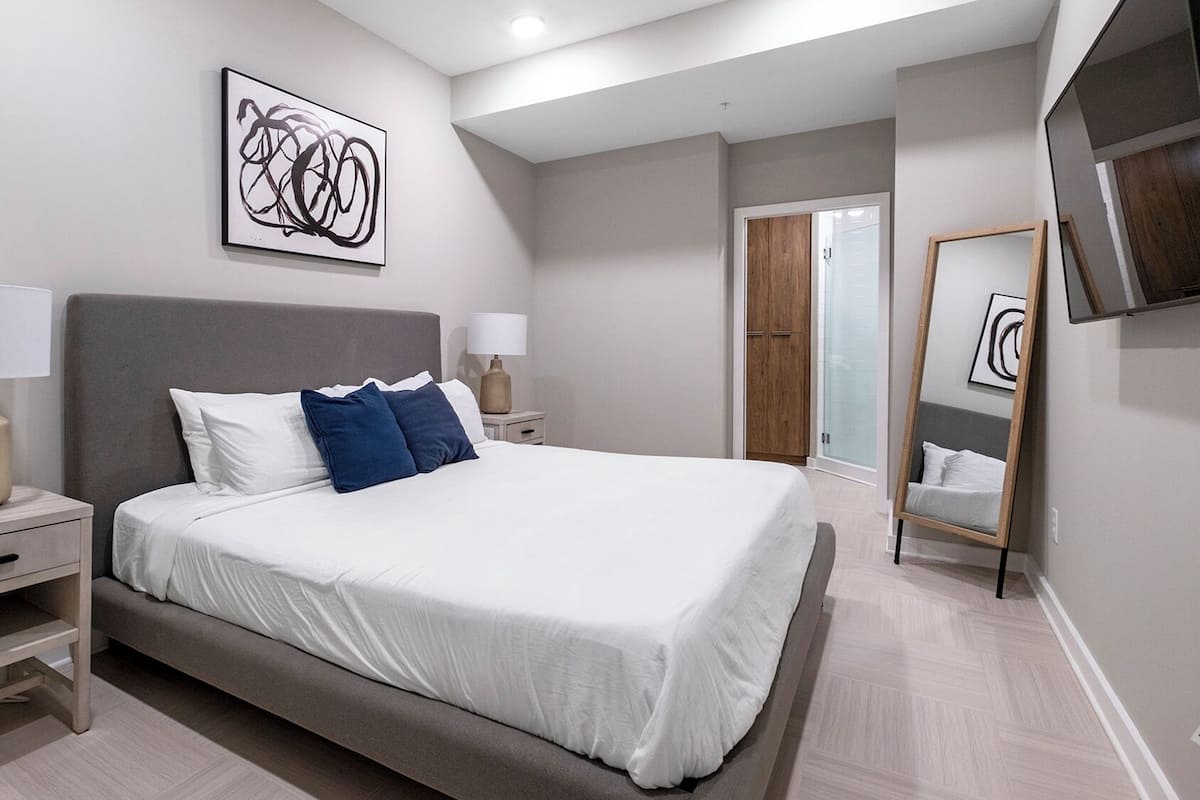 Un dormitorio moderno con una cama grande, mesitas de noche, un espejo y un cuadro en la pared.