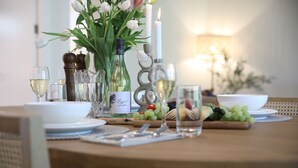 Une table à manger dressée avec de l’argenterie blanche, des verres et une bouteille de vin blanc, entourée de fleurs fraîches et de fruits.