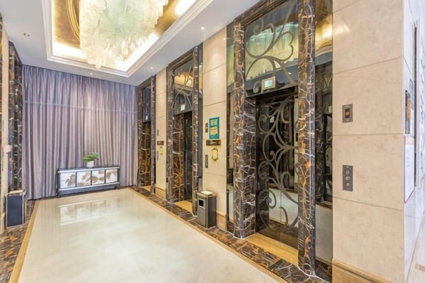 A hotel lobby with marble floors, a long corridor, and two elevators with ornate designs.