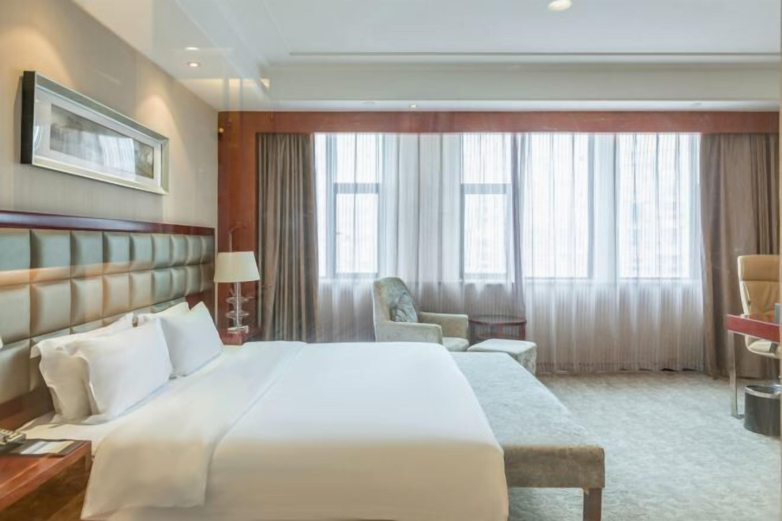A hotel room with a large bed, a desk, a chair, and a window with curtains.