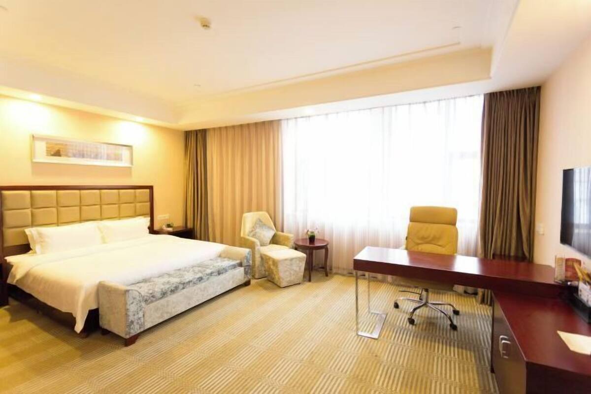 A hotel room with a bed, two armchairs, a desk, and a television.