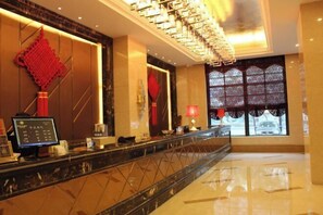 A hotel reception area with a marble counter, a digital display, and a large window with patterned curtains. - Guomao Hotel (Yichang)