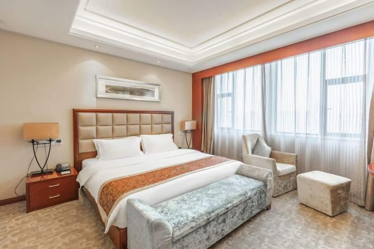 A hotel room with a large bed, a bench, a chair, and a small ottoman.