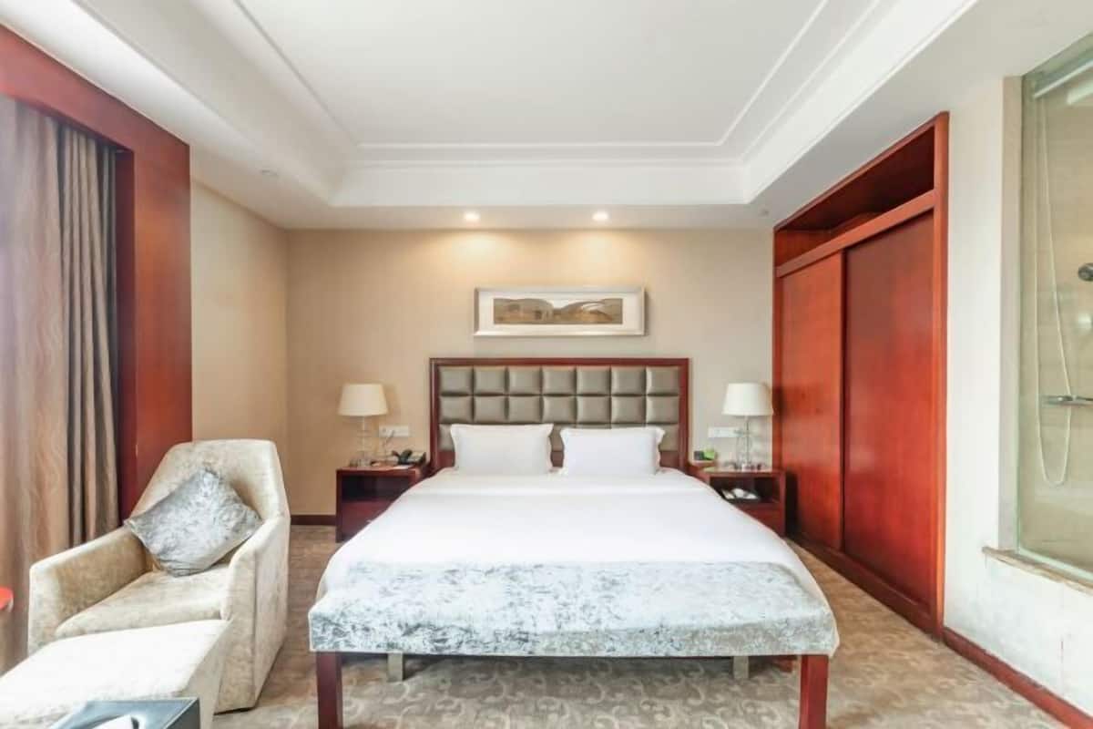 A hotel room with a large bed, a chair, a nightstand, a lamp, and a framed picture on the wall.